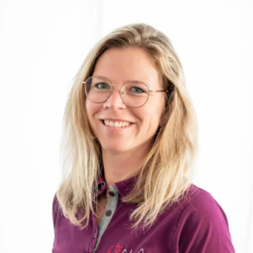 Frau mit schulterlangem, blondem Haar tr&auml;gt ein lila Poloshirt mit grauem Kragen und Logo auf der Brust.